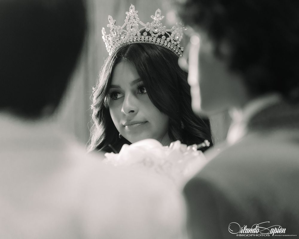 A close-up black and white portrait of someone wearing an ornate tiara and smiling.