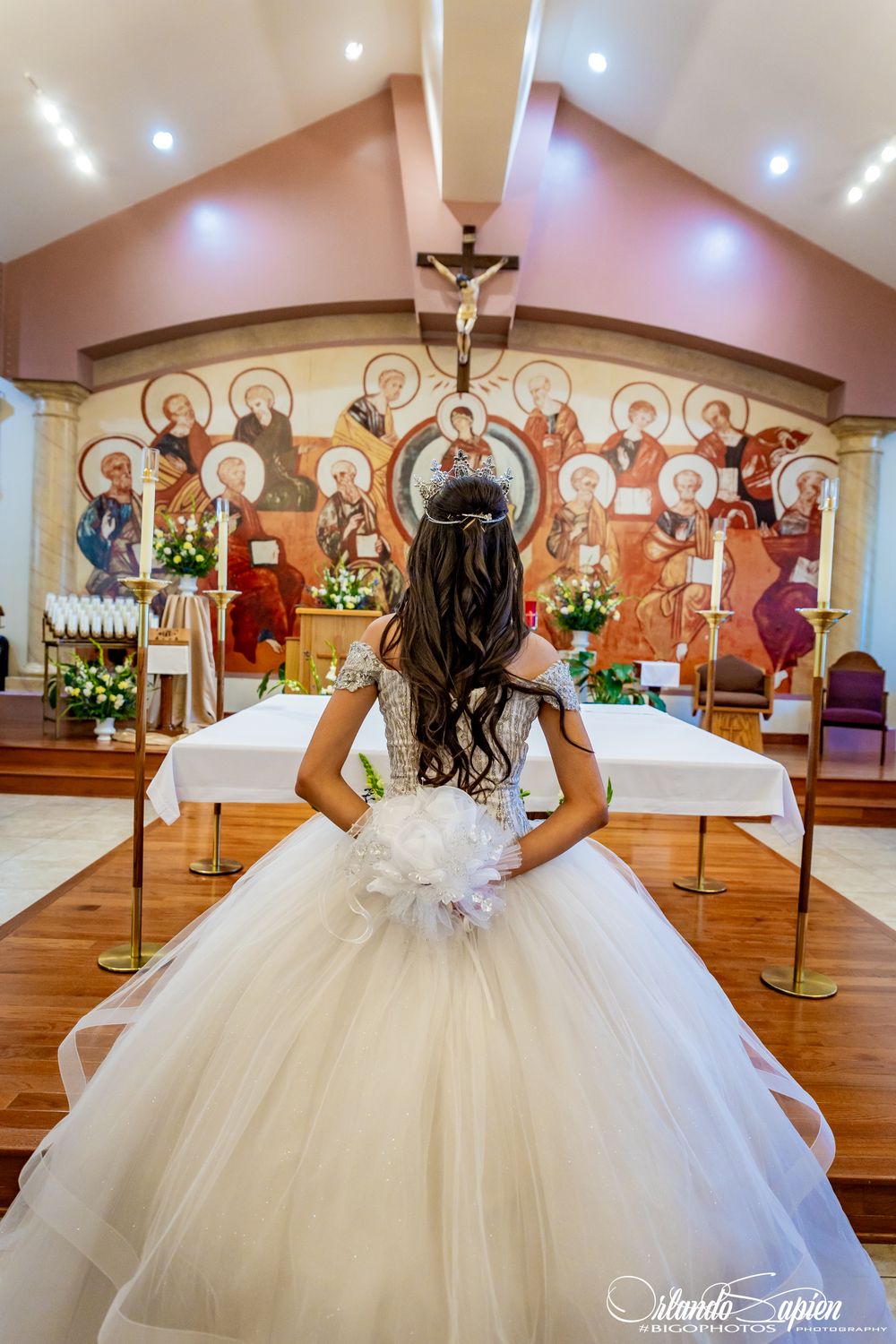 A flowing white ball gown photographed in a church with religious artwork on the walls.
