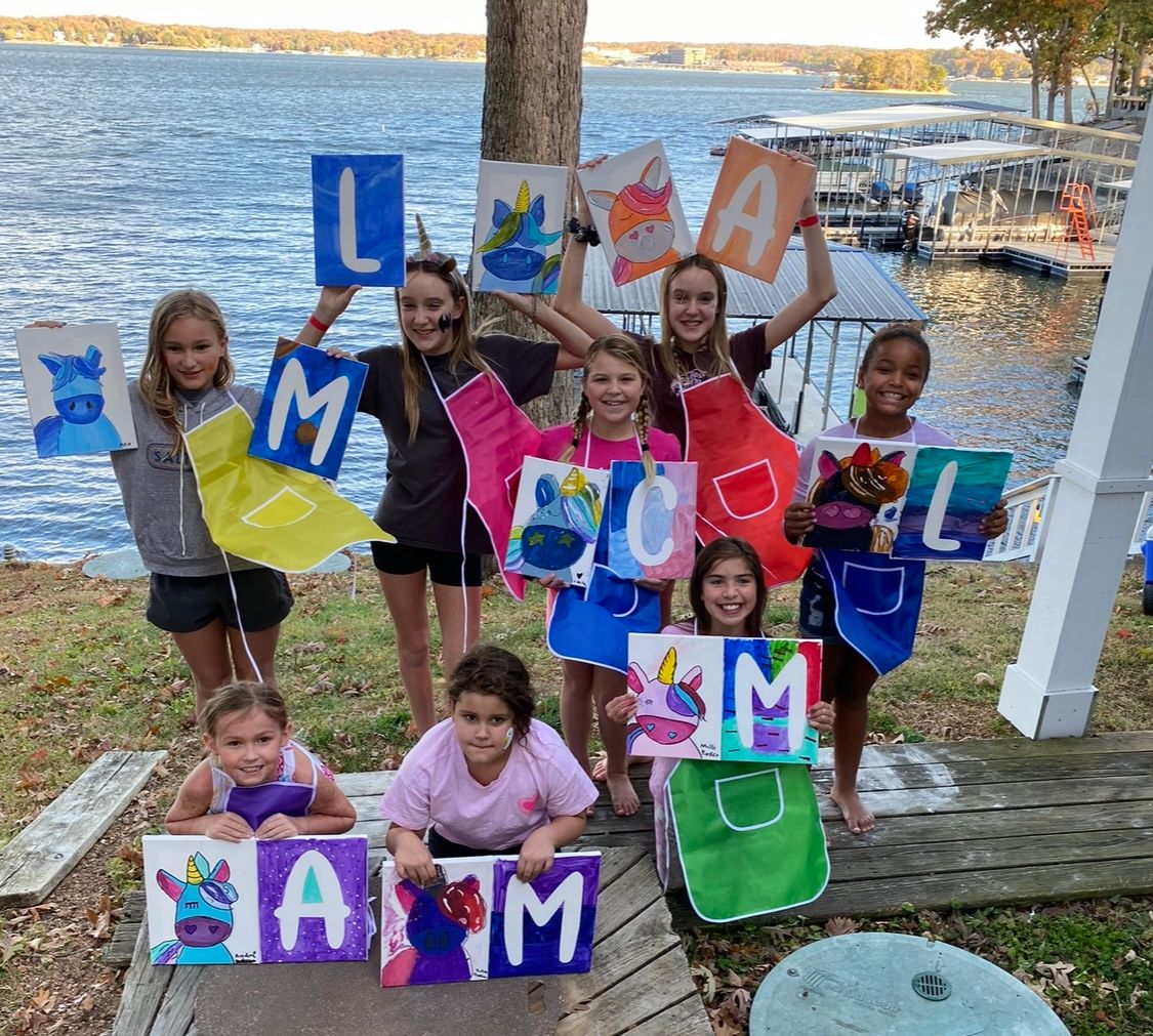 People displaying colorful letter-themed art projects by the waterfront.