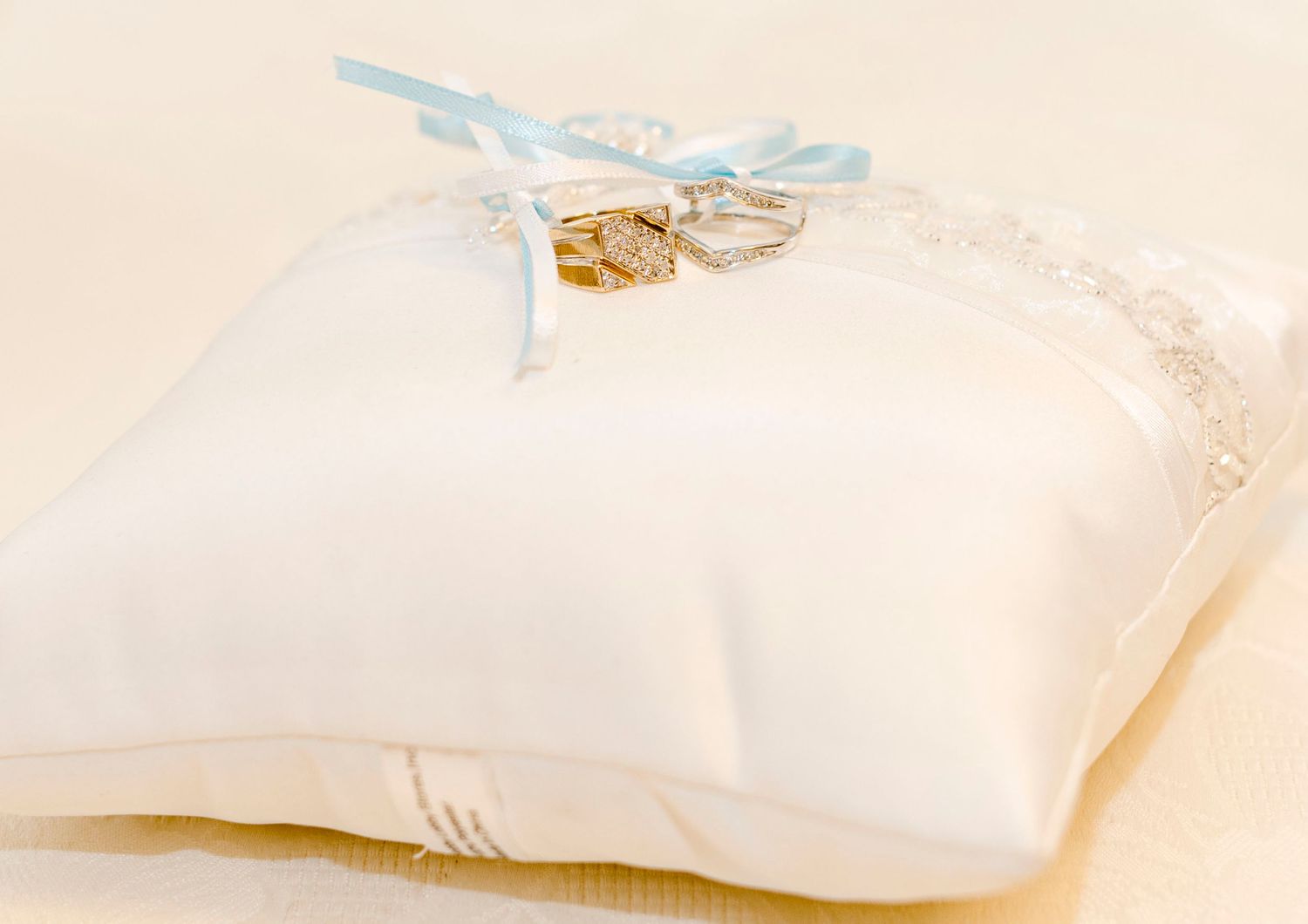Wedding rings tied with blue ribbon rest on white satin ring bearer pillow.