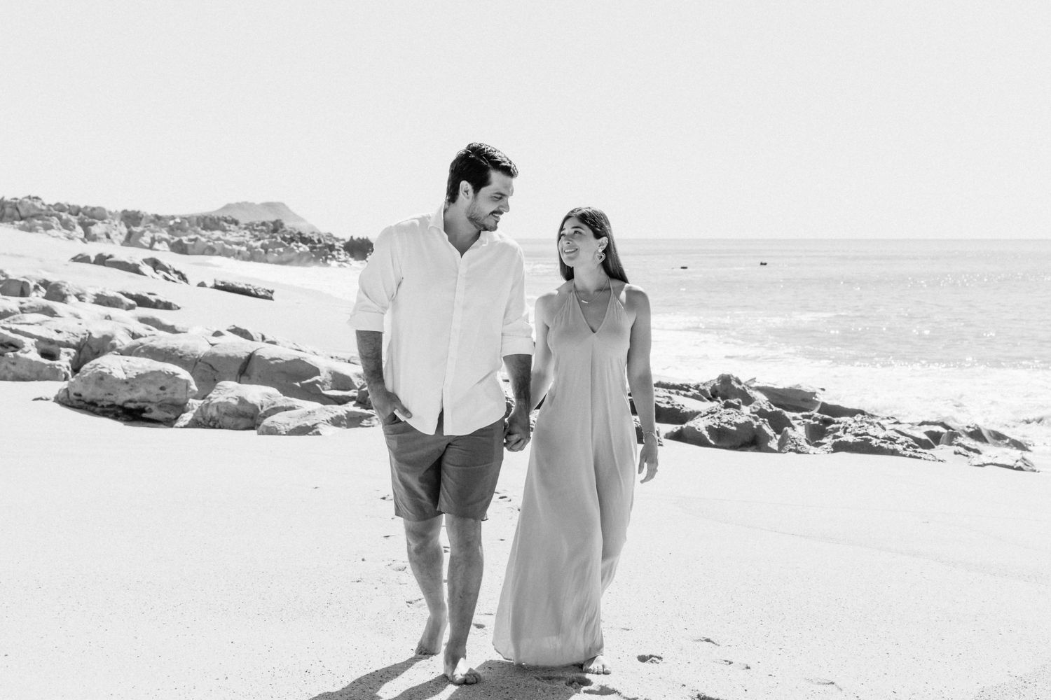 Couple walking along rocky beach coastline in black and white photograph.