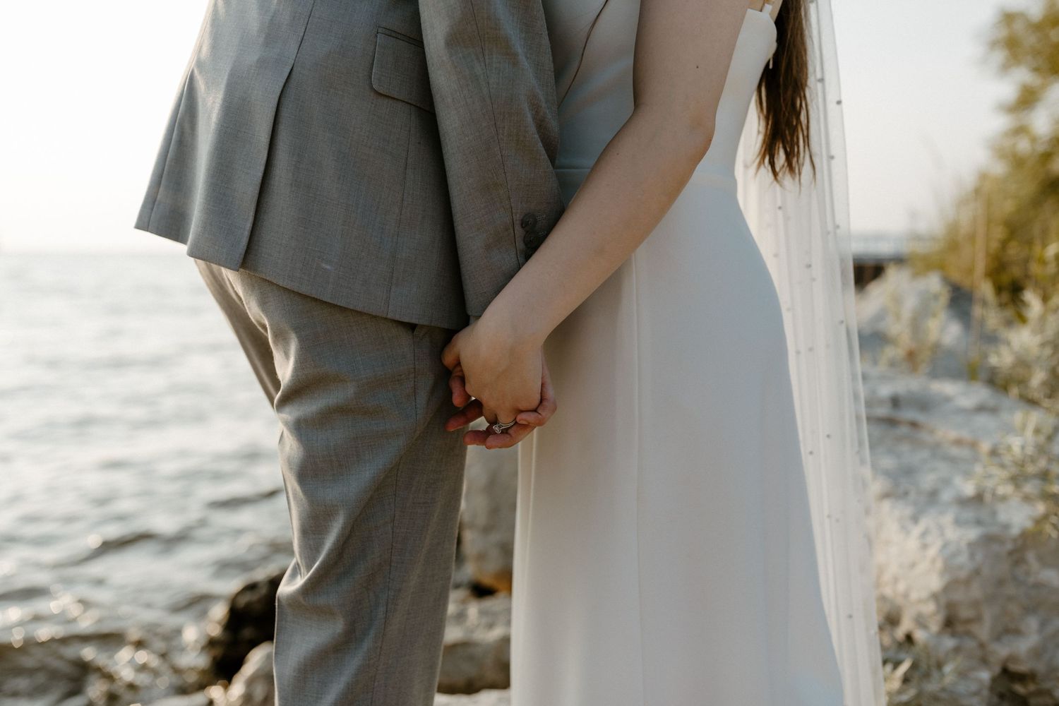 A couple holding hands while standing on a rocky shore near a body of water. Fort Worth Texas wedding photographer.