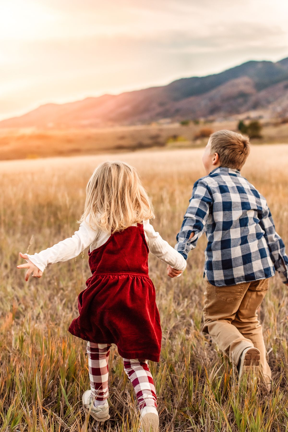 Siblings in grassy field at South Valley Park running towards a mountain sunset.