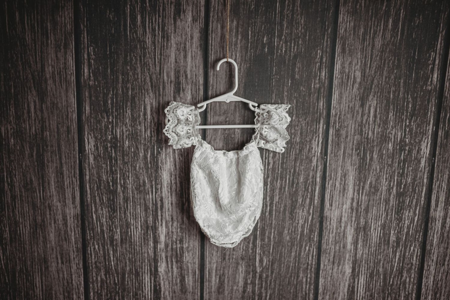 White lace baby dress hanging against dark wooden background.