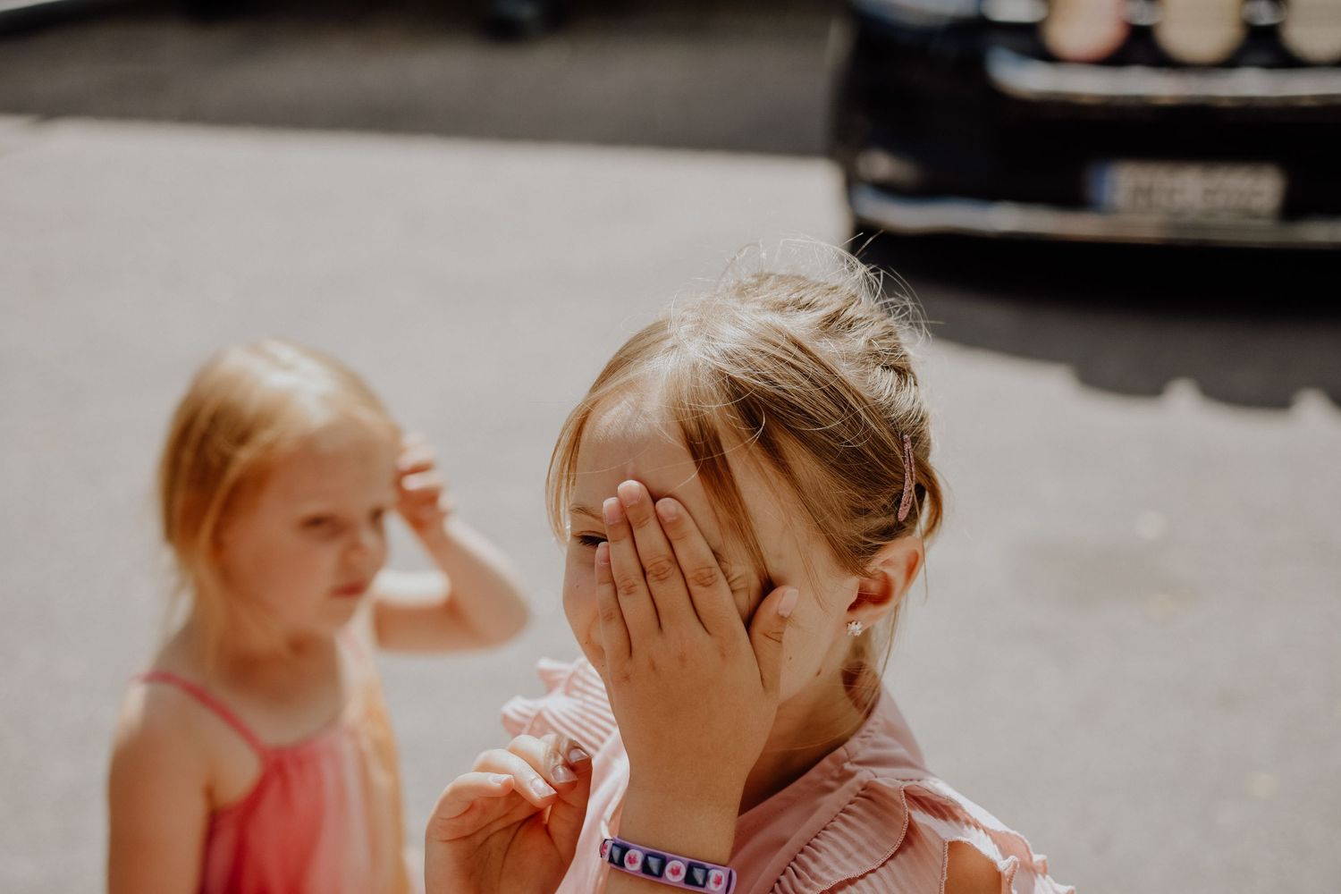 Two children playing together, with one covering their face with their hands.