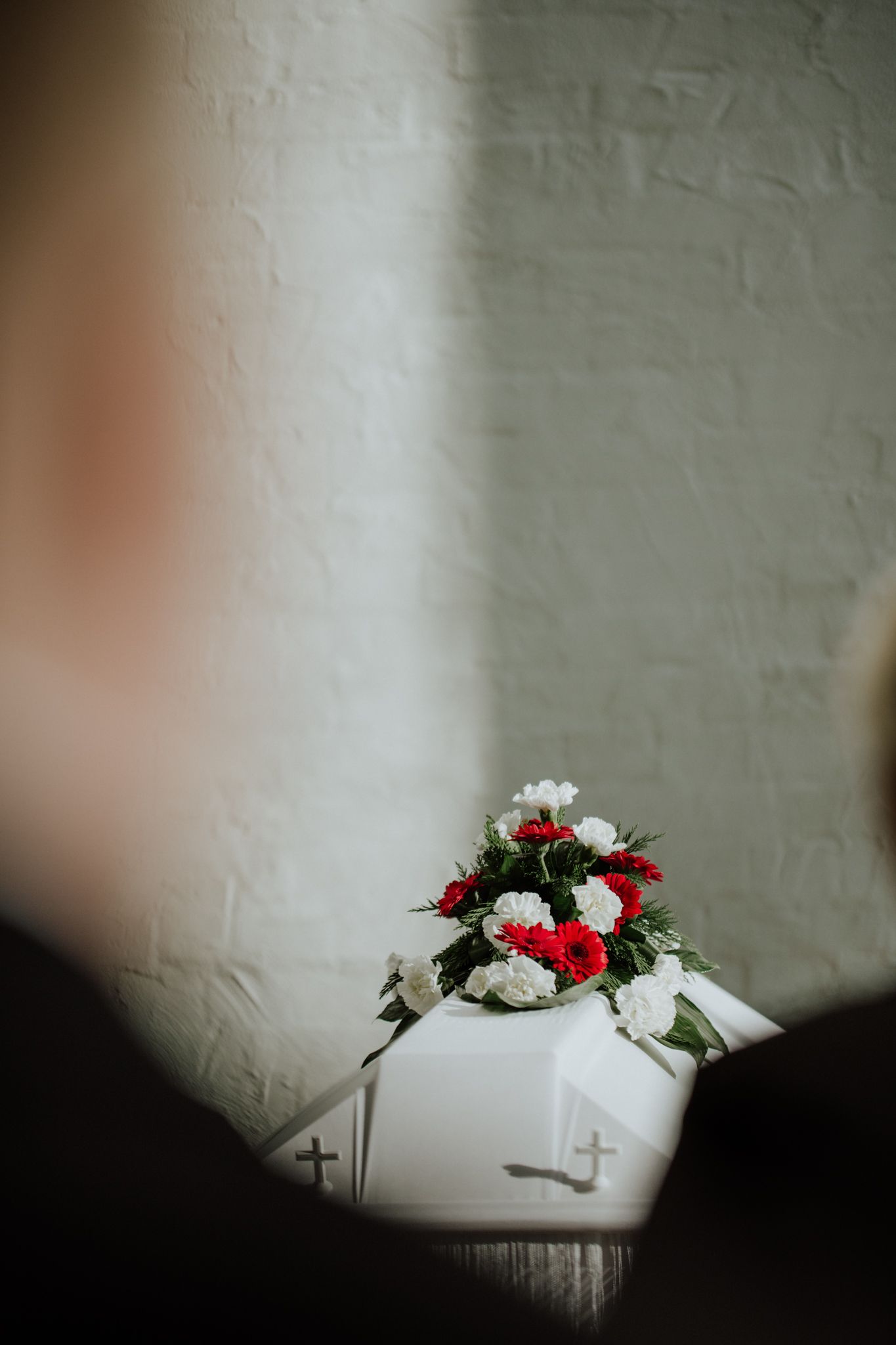 Red and white floral arrangement on white surface against textured wall.