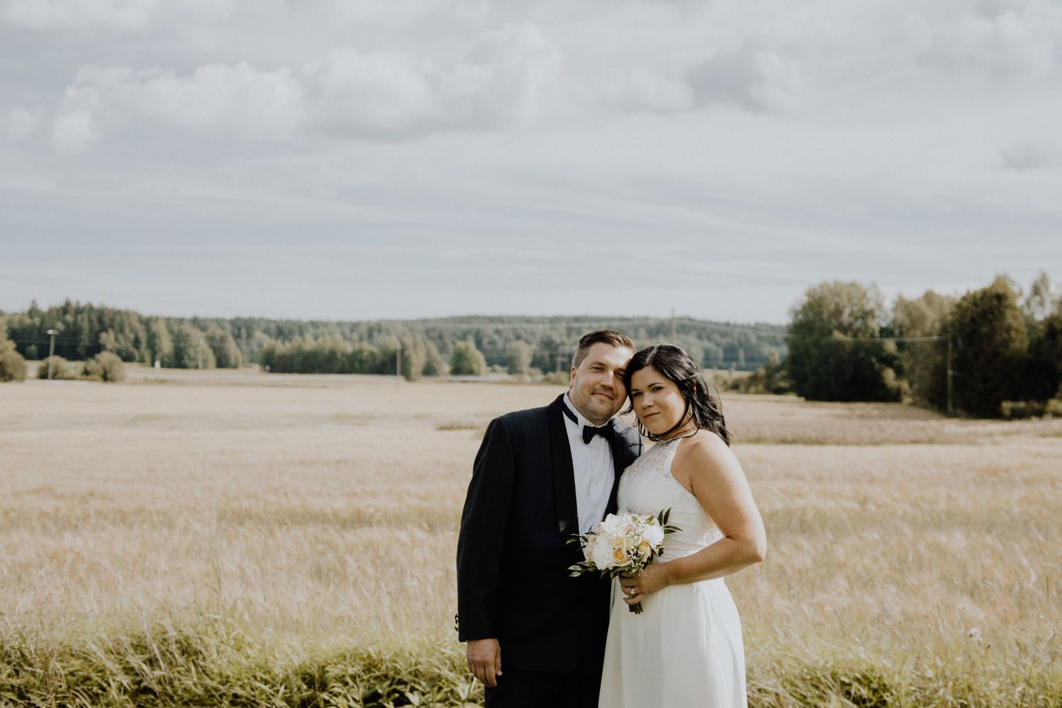 A wedding couple standing together in a sunlit meadow with forest in background.