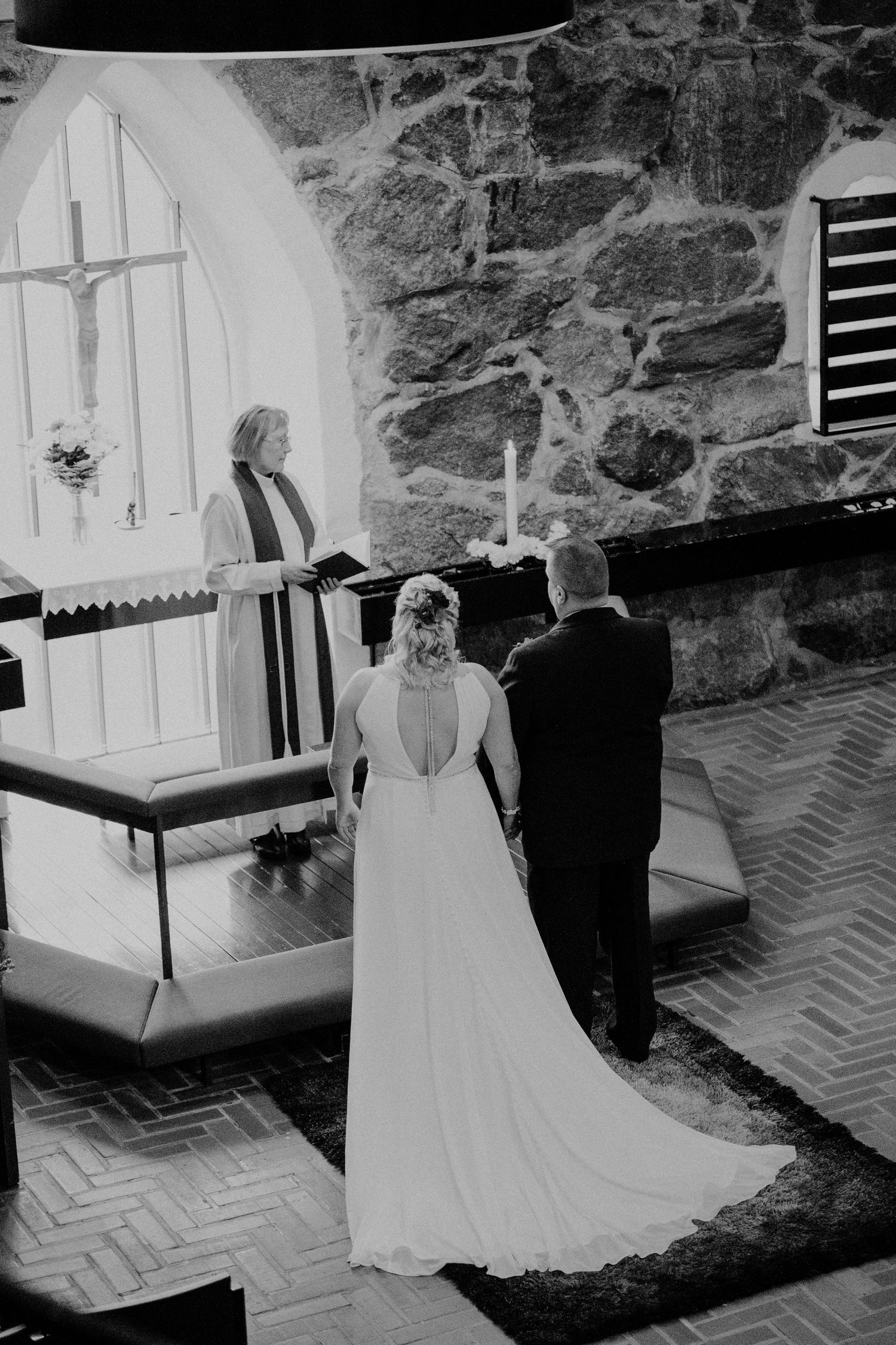Black and white photo of a wedding ceremony in a stone church with arched windows.