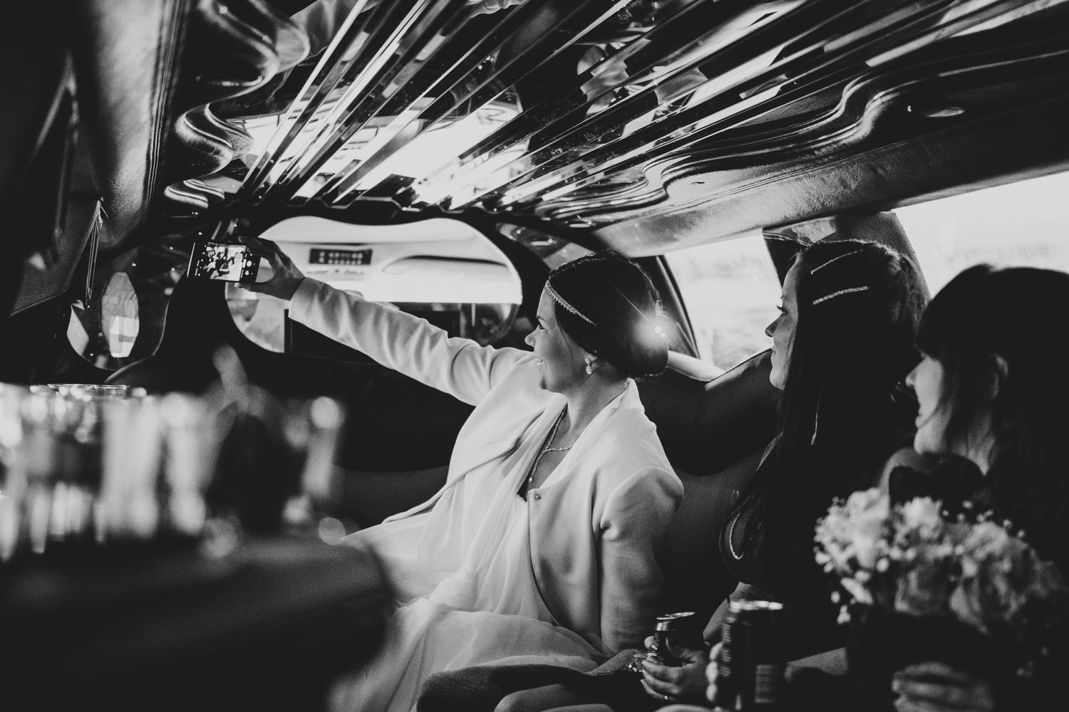 Black and white photo of a couple in the back of a vintage car during their wedding celebration.