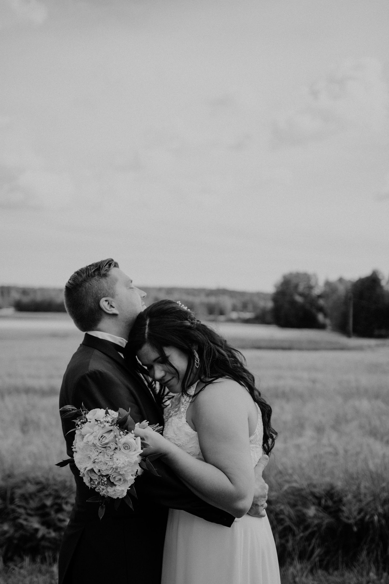 An intimate black and white portrait of a couple embracing in a field.