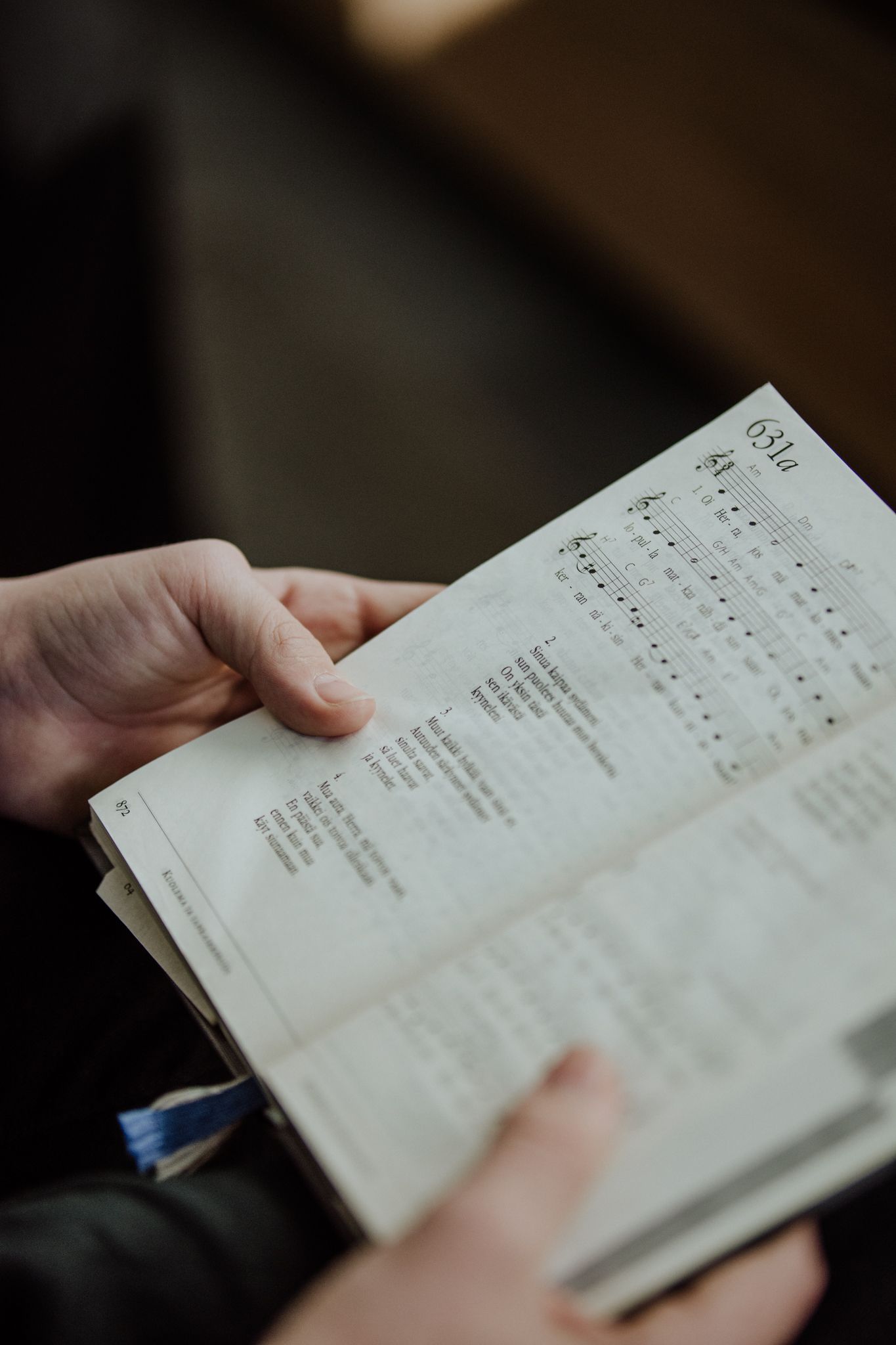 Hands holding open hymnal or prayer book with text visible on pages.
