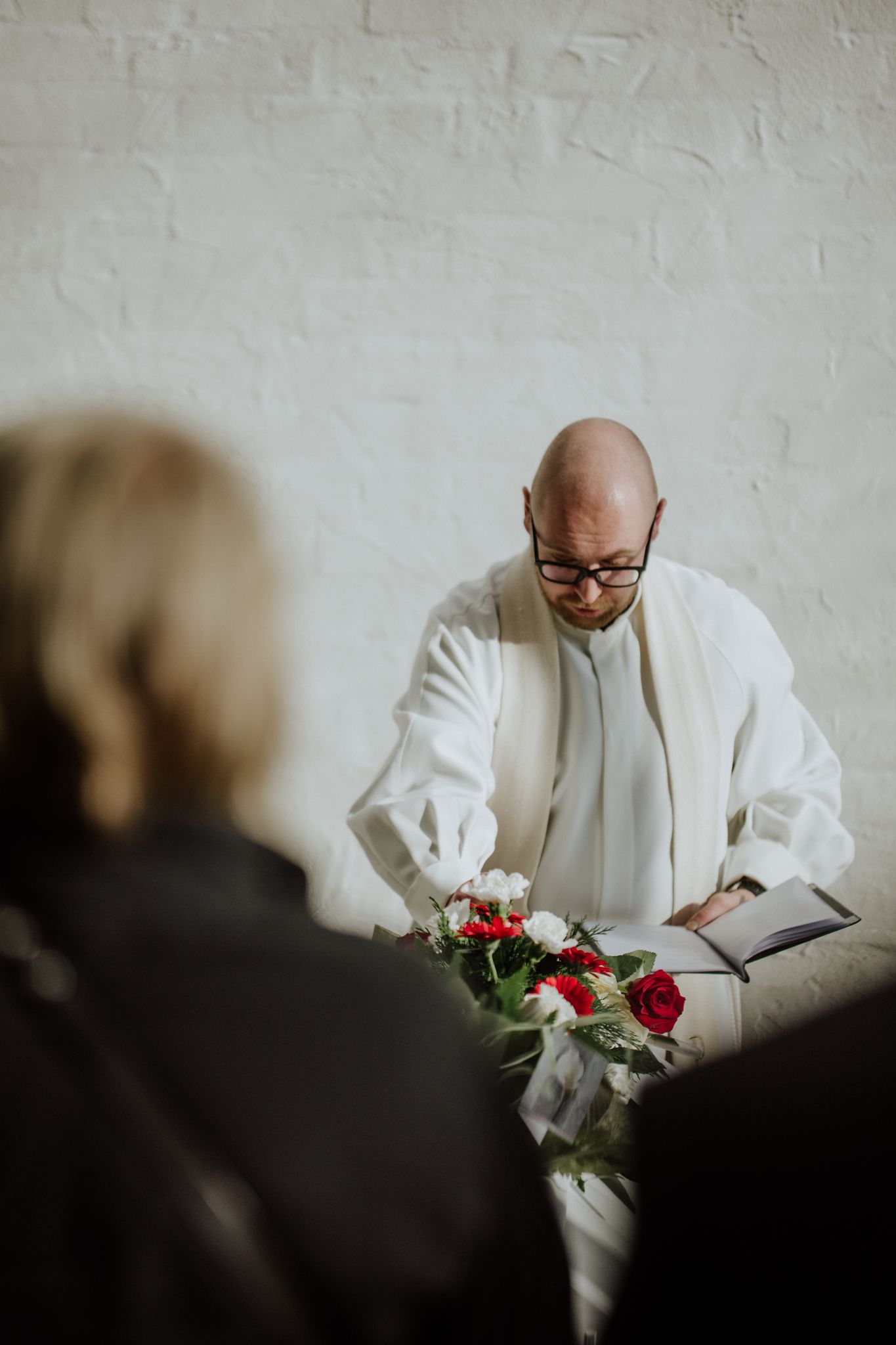 Religious figure in white robes reading from book during ceremony.