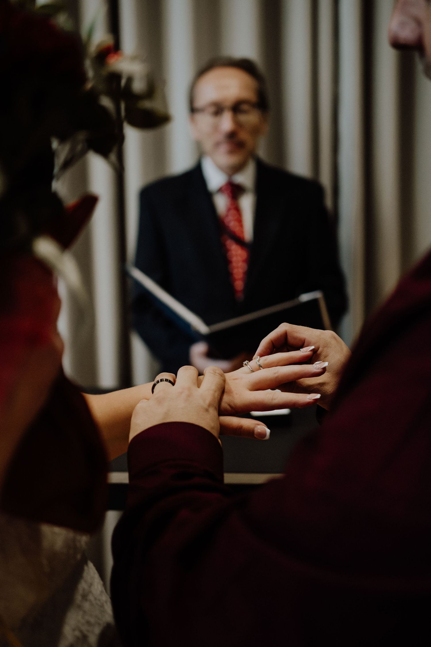 Close up of hands exchanging rings during a wedding ceremony with an officiant in the background.