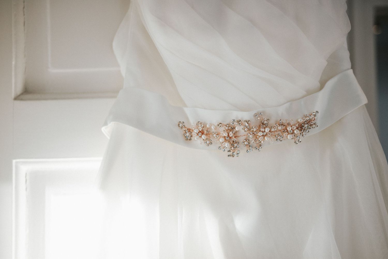 Delicate beaded detail on a white wedding dress belt captured in natural window light.