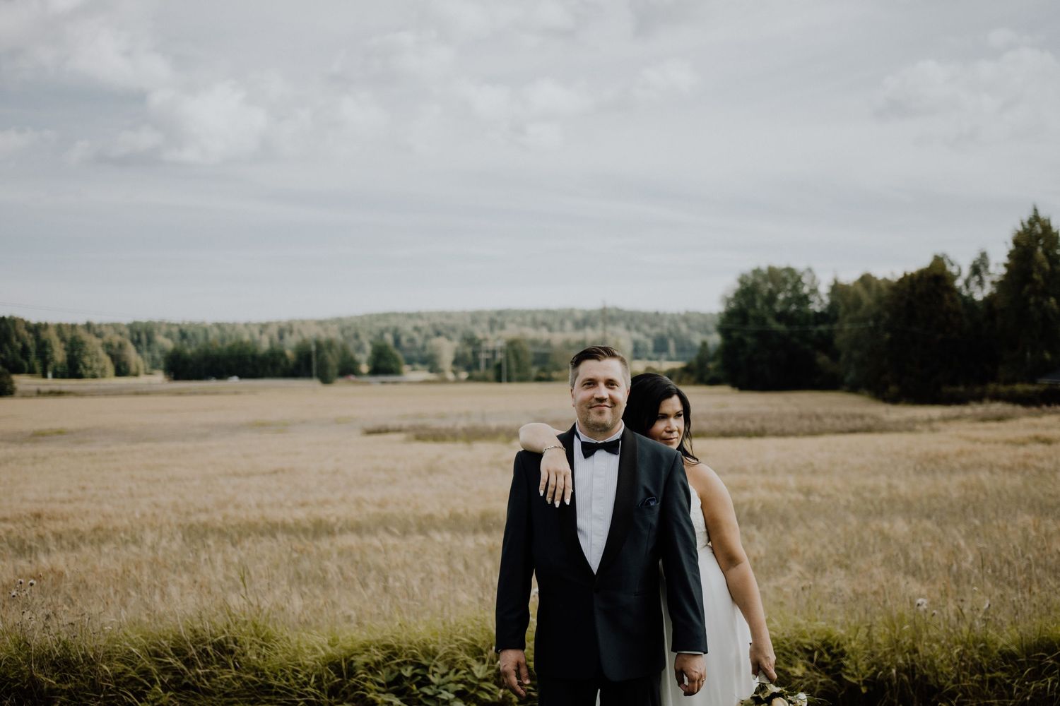 A wedding couple standing in a vast open field on an overcast day.