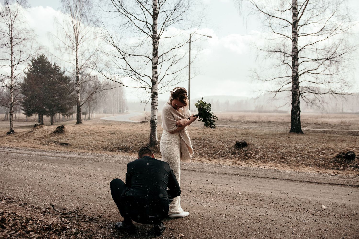 Winter wedding proposal scene on a misty path surrounded by bare trees.