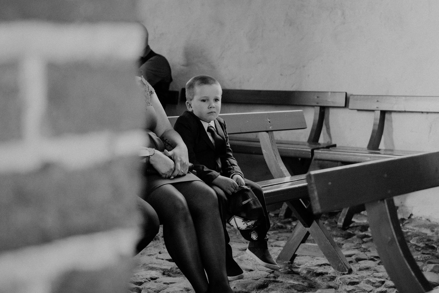 A small child sits on a wooden bench in formal attire, captured in black and white.