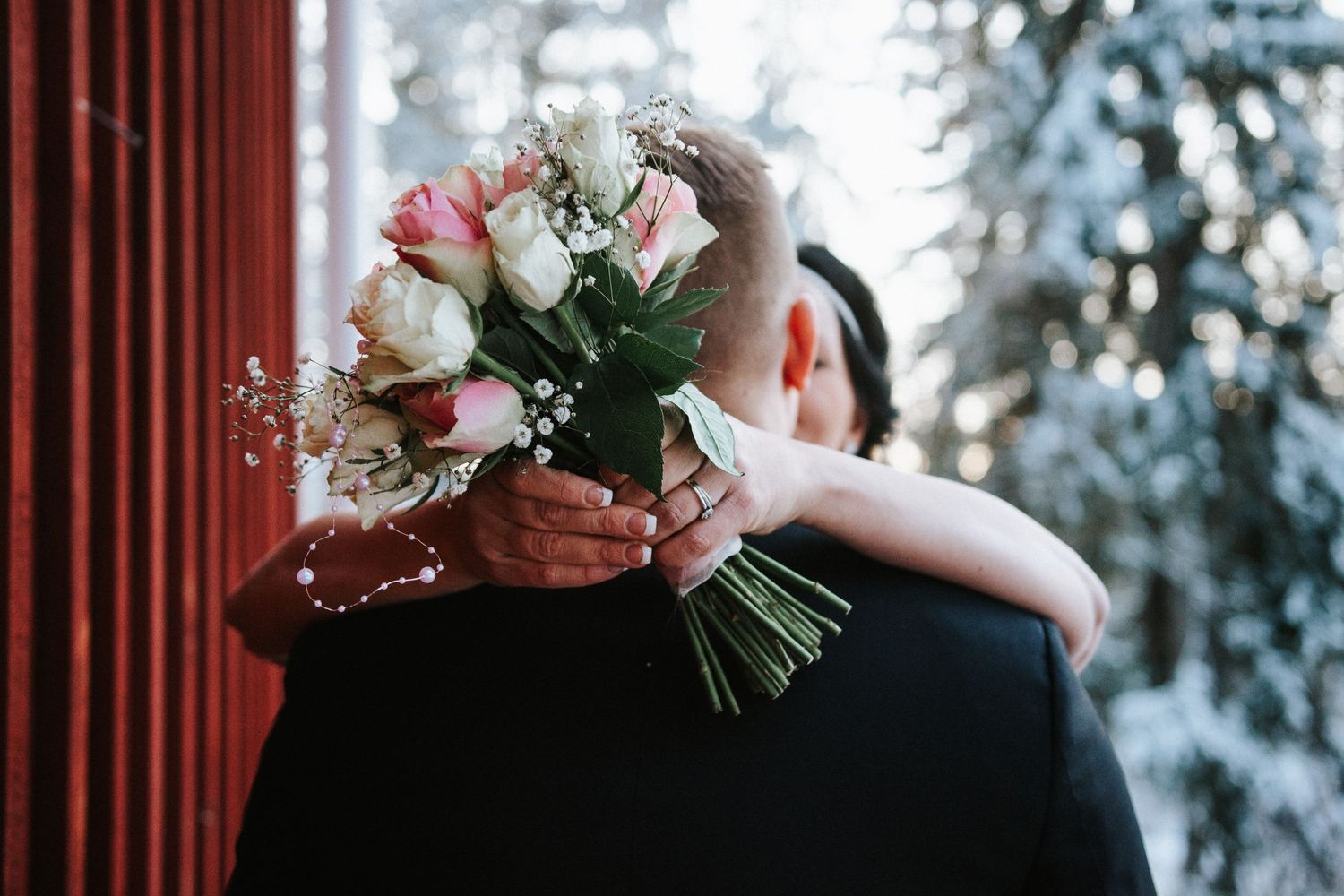 Close-up shot of a wedding bouquet with roses while couple embraces.