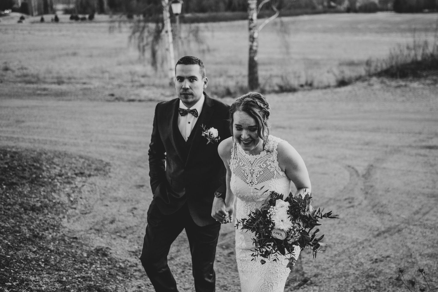 Couple walking together in formal wedding attire through a scenic field.