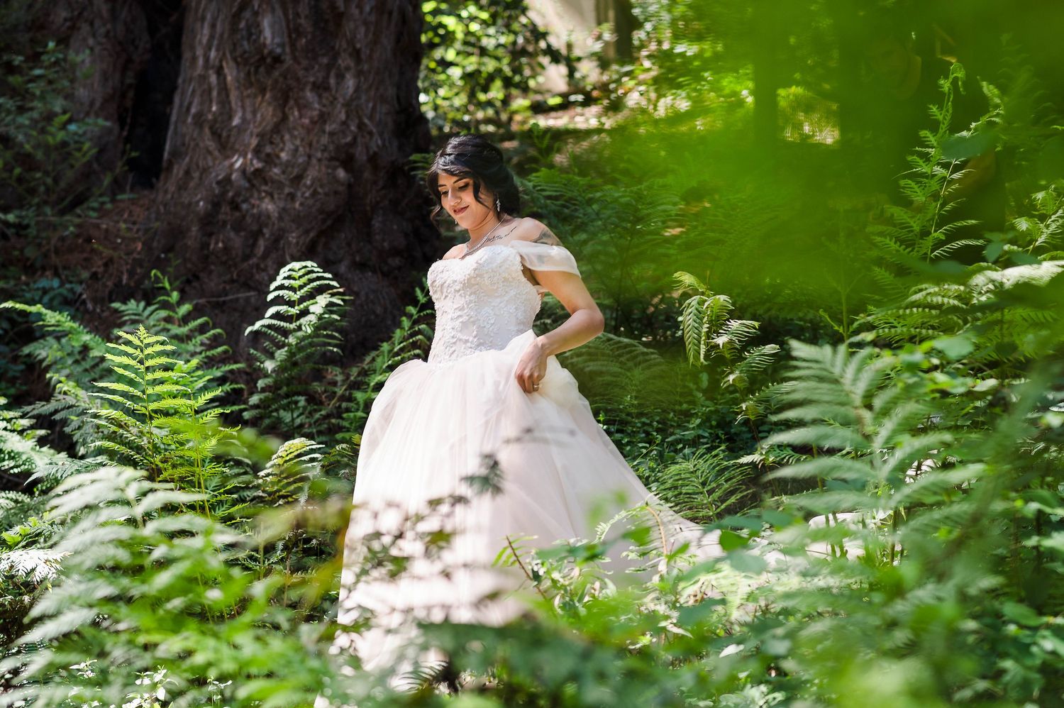 A flowing white wedding gown photographed in a lush forest setting with ferns.