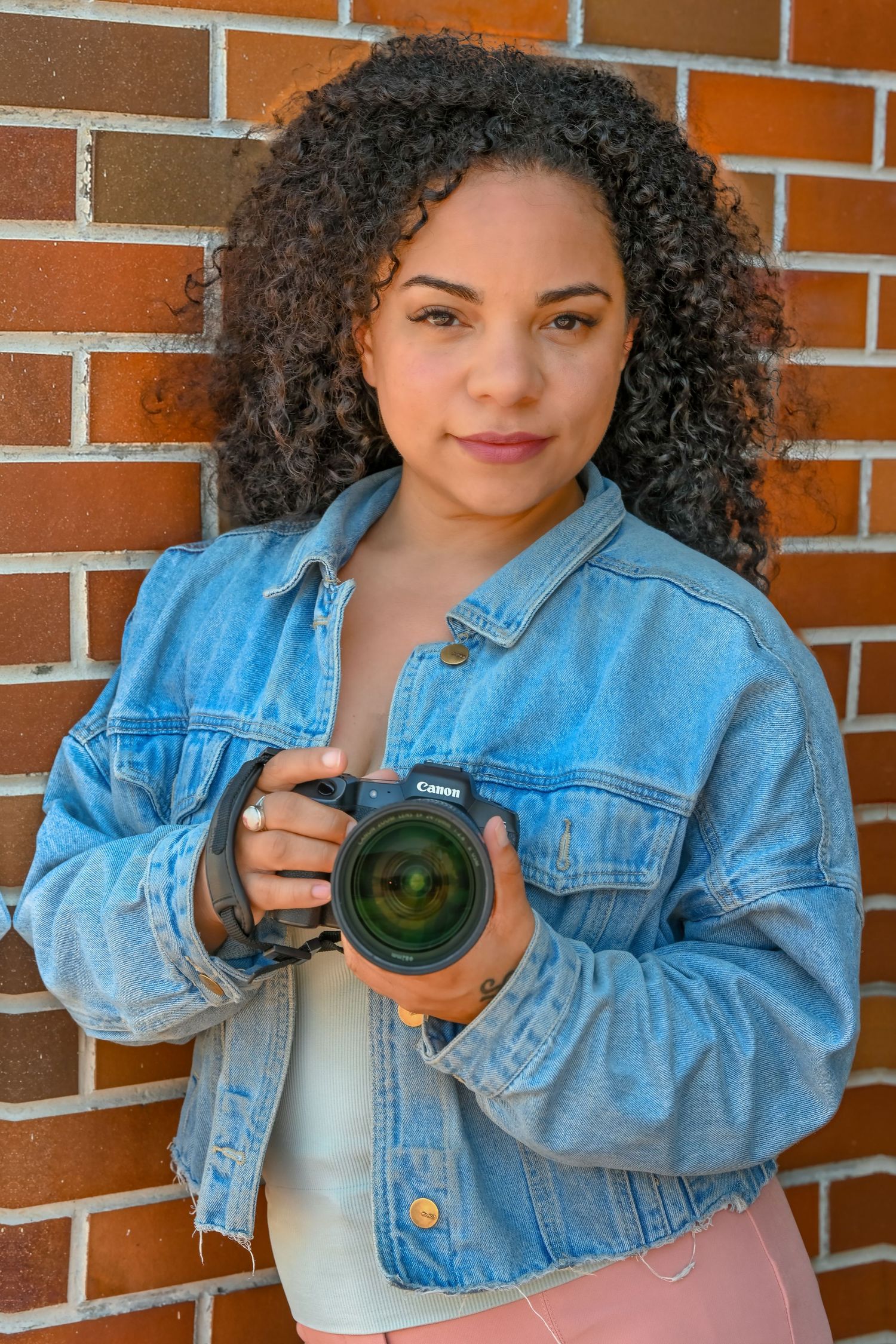 A photographer wearing a denim jacket demonstrates different camera angles against a brick background.