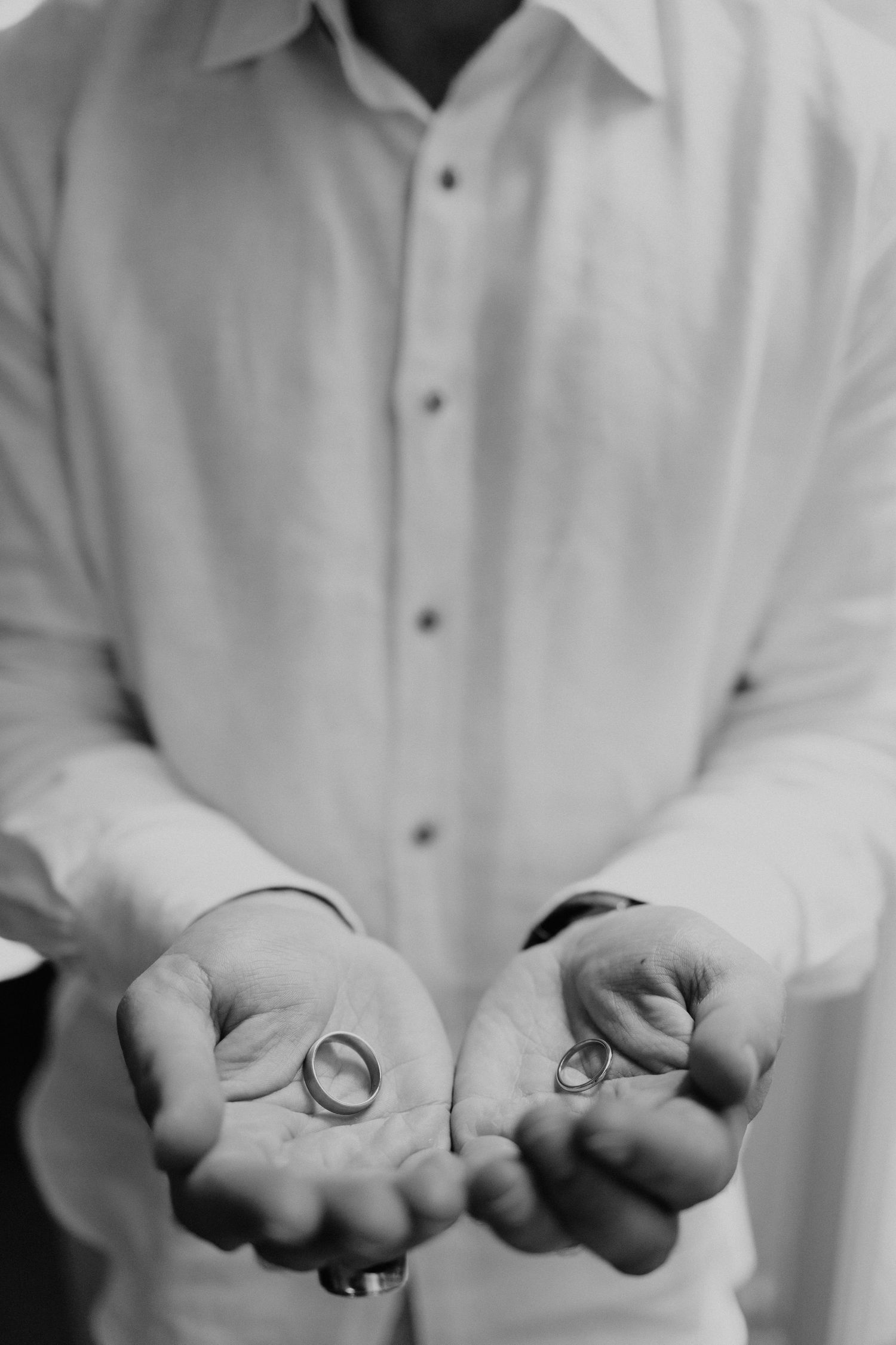 Close-up of hands holding wedding rings in black and white.