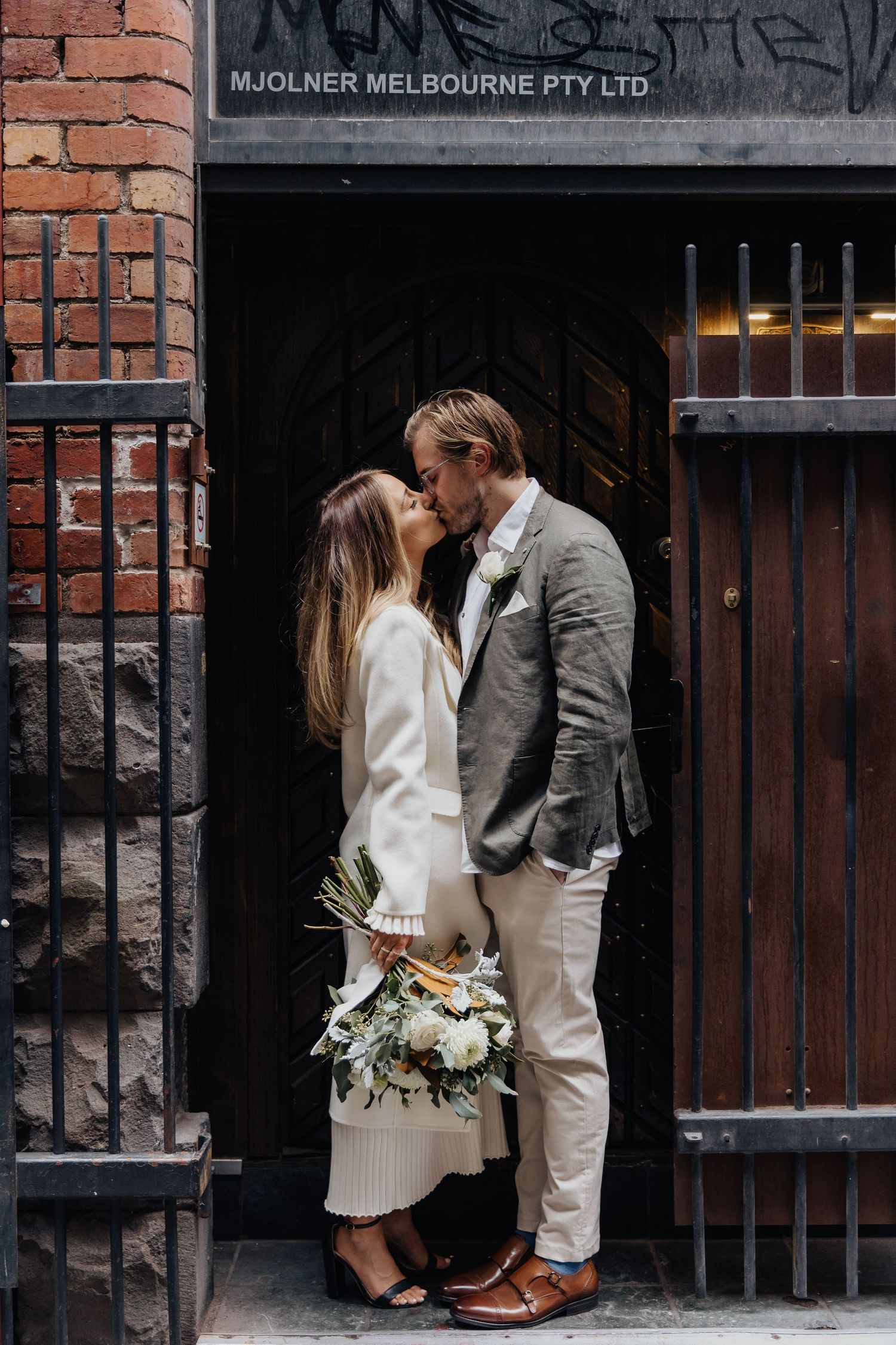 Couple in wedding attire sharing intimate moments against industrial brick wall backdrop.