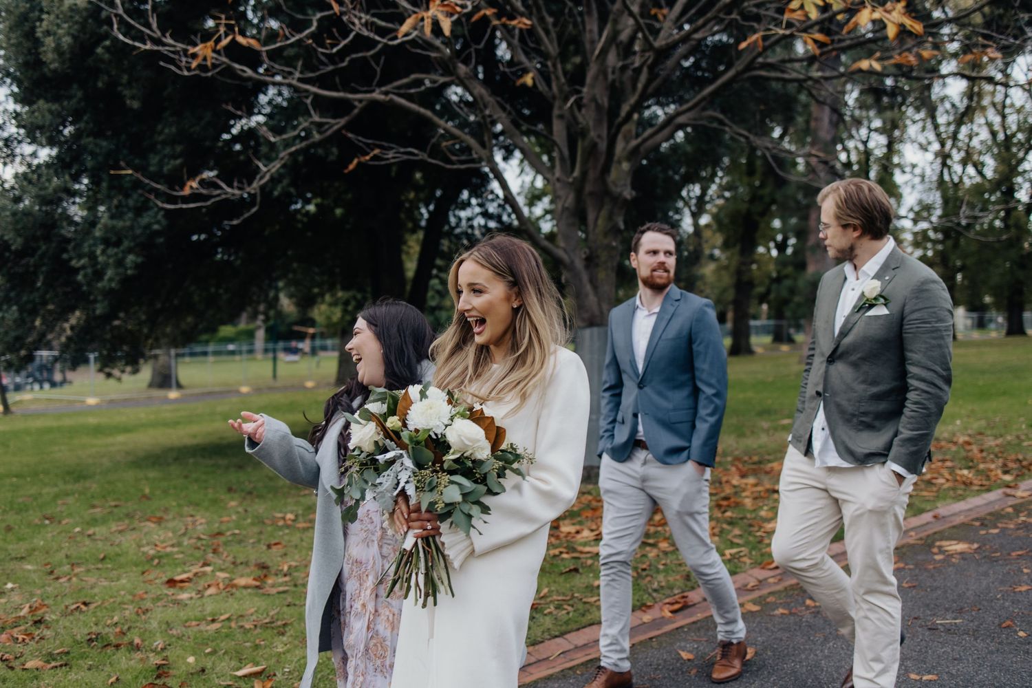 Wedding party walking through an autumn park with fallen leaves on the ground.