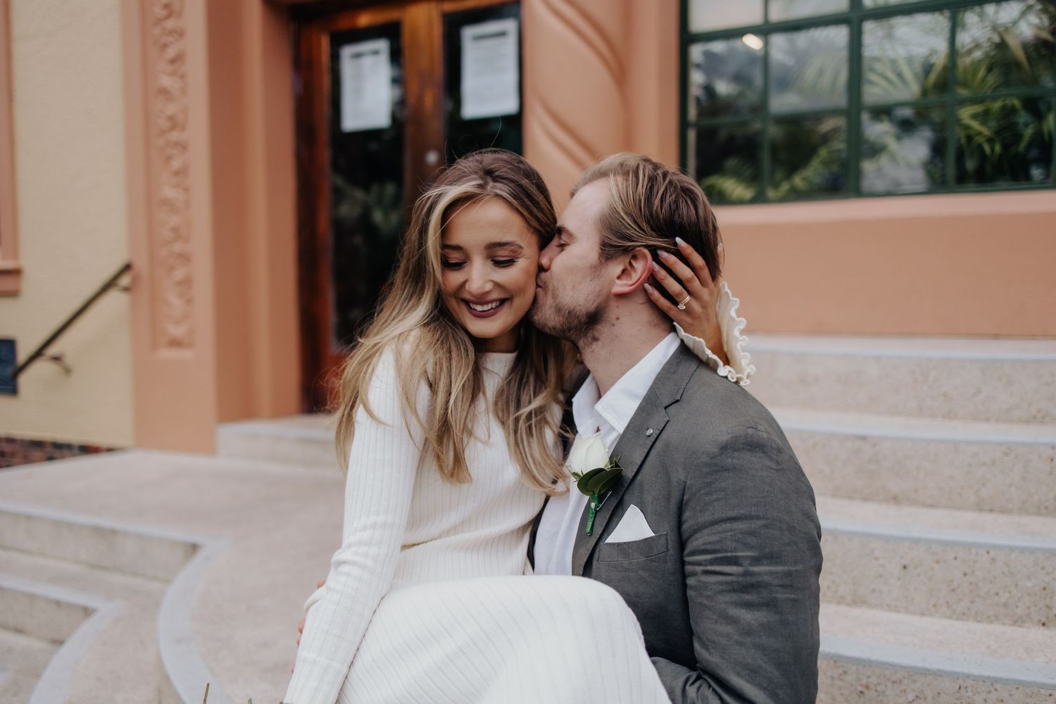Couple sharing intimate moment on peach-colored steps of building.