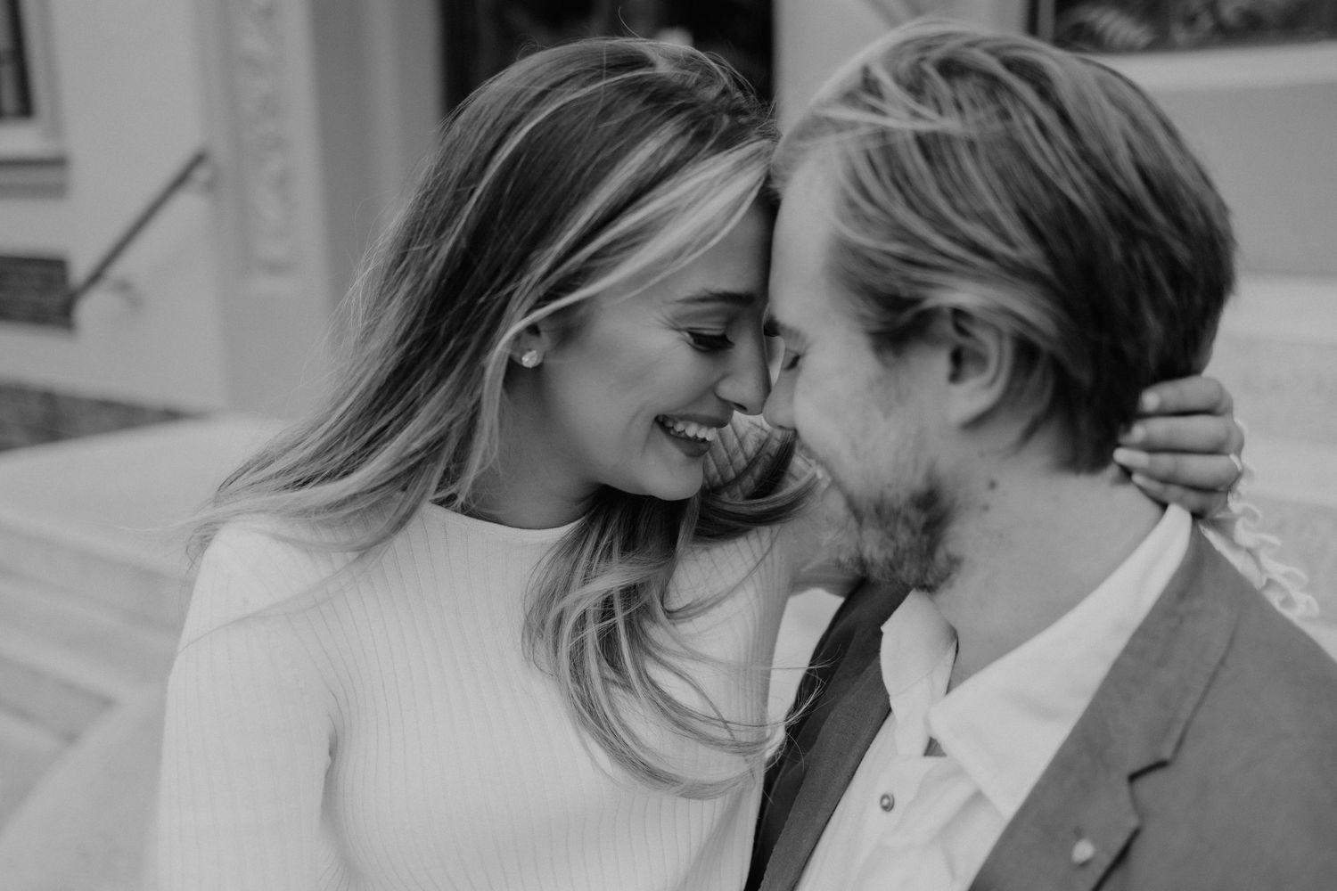 A romantic couple shares an intimate moment against a wall in black and white.