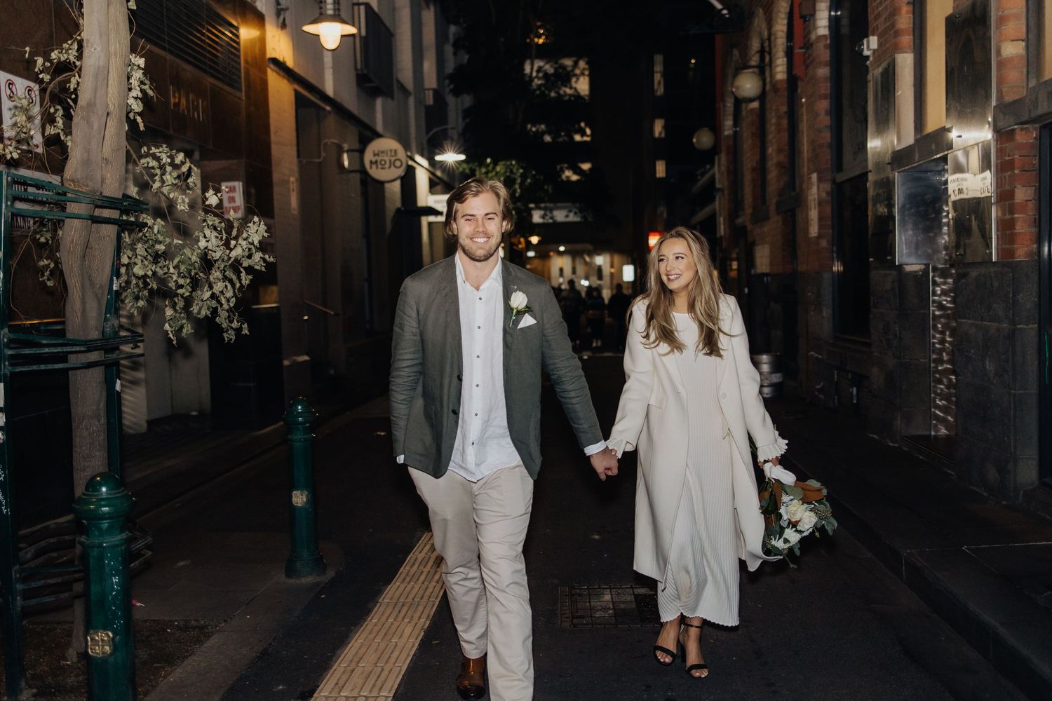 A stylishly dressed couple walking together on a city street at night.