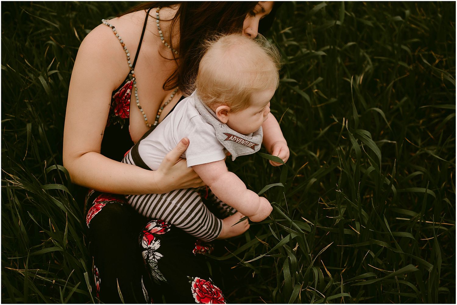 Baby in white top and striped pants sits supported in a flowery summer dress.
