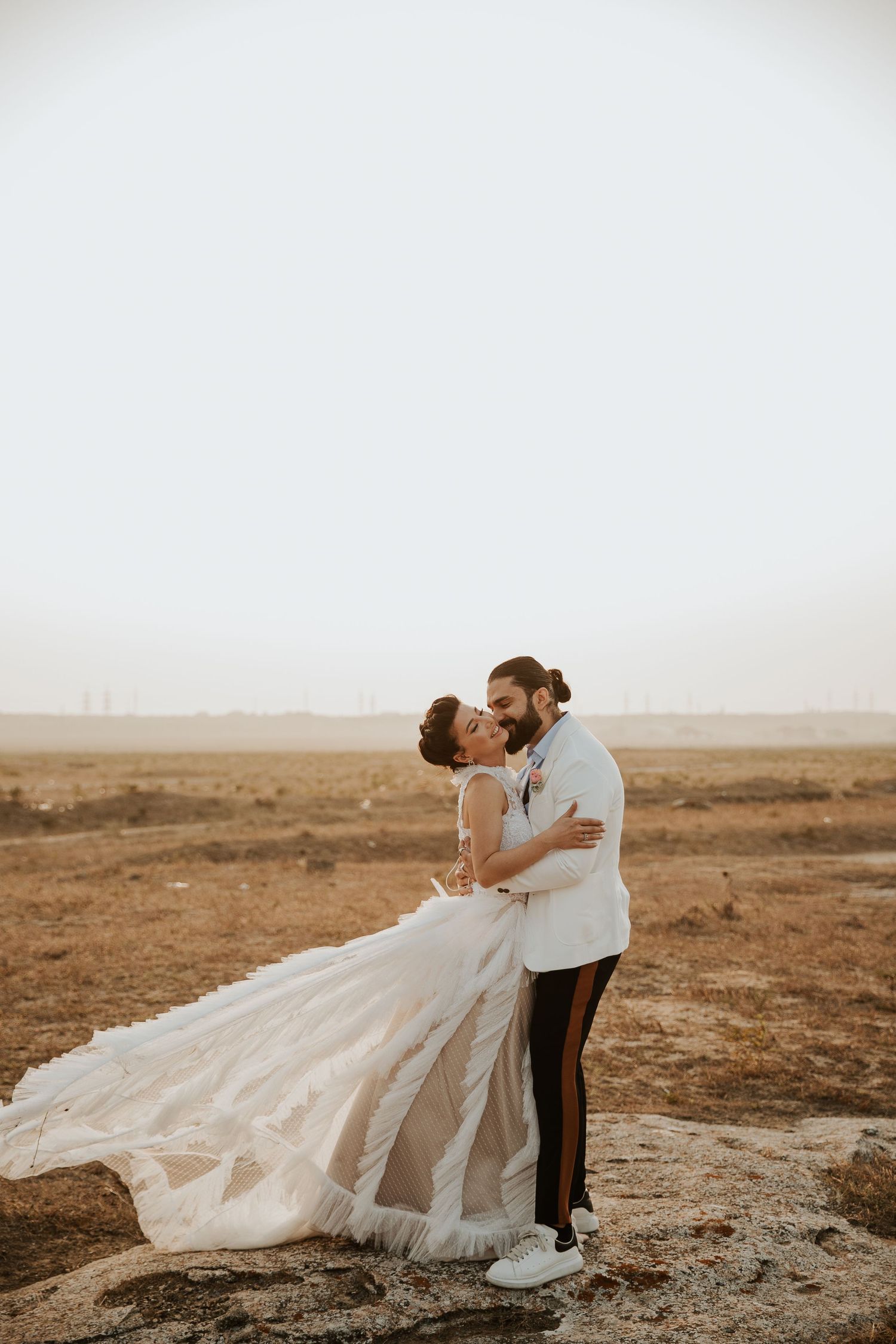 Romantic desert wedding portrait with flowing white dress against arid landscape.