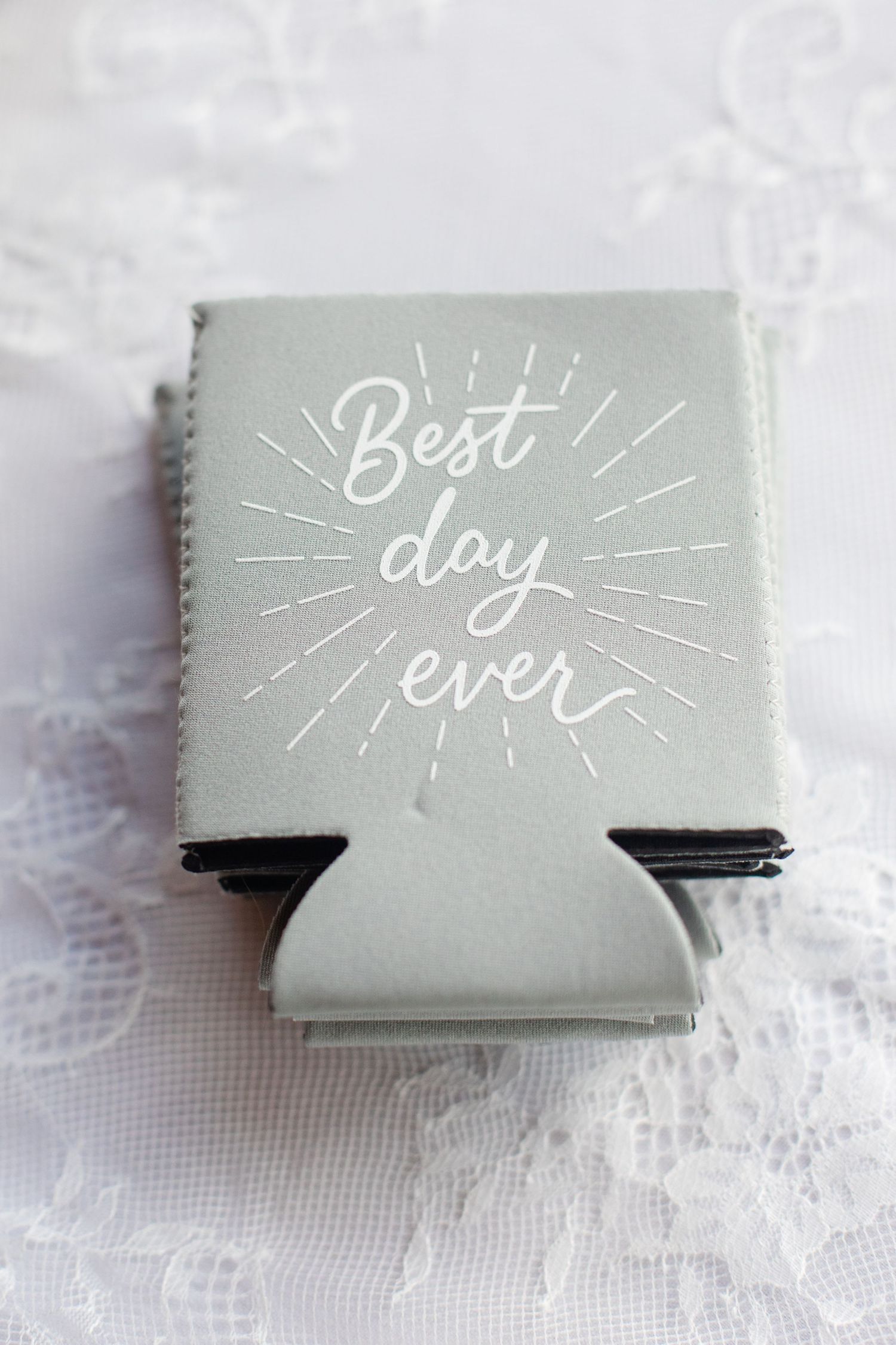 Light gray wedding favor koozies with 'Best day ever' text in white calligraphy.