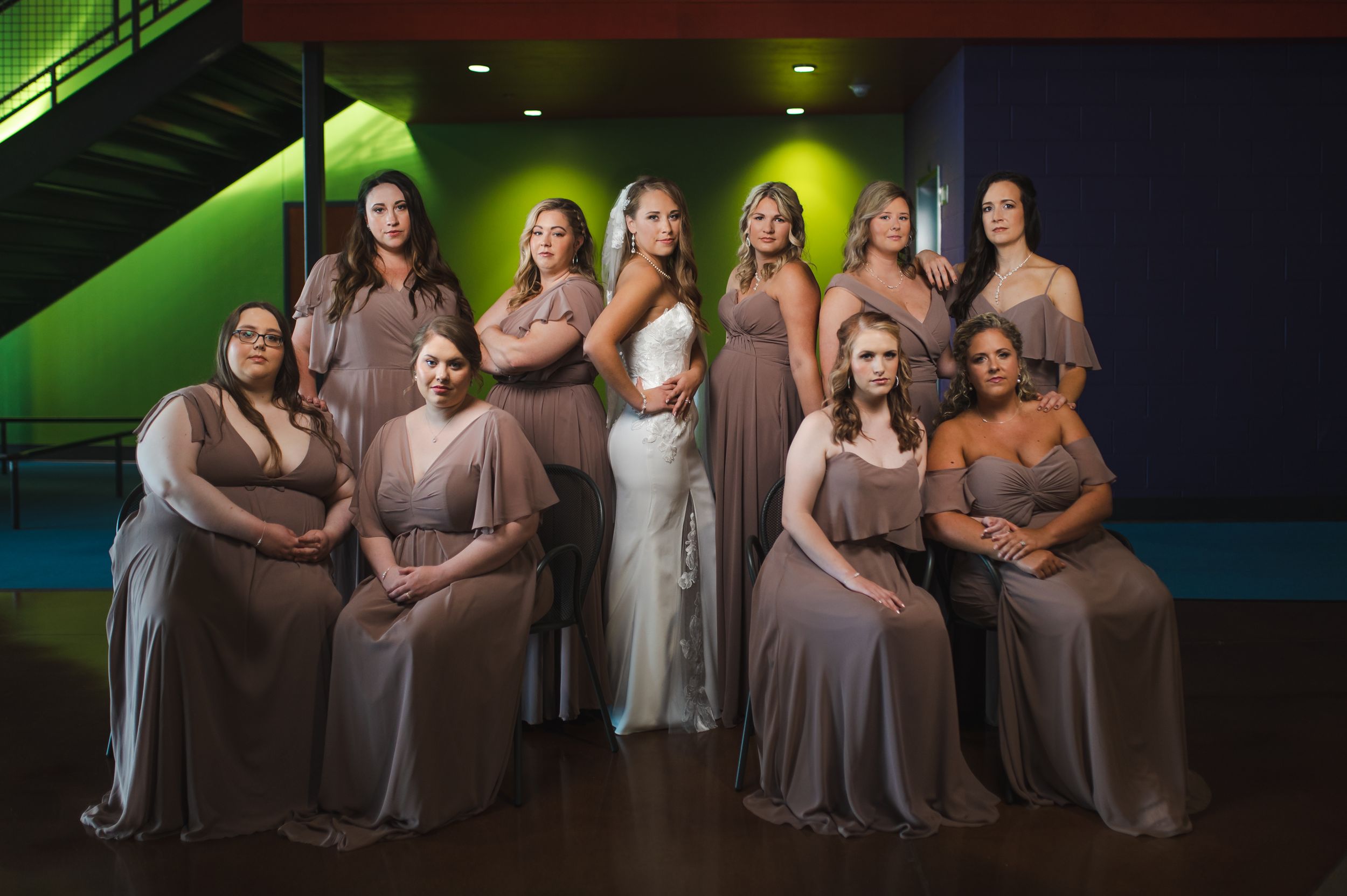 Bridesmaids in neutral dresses pose under dramatic green lighting at reception venue.