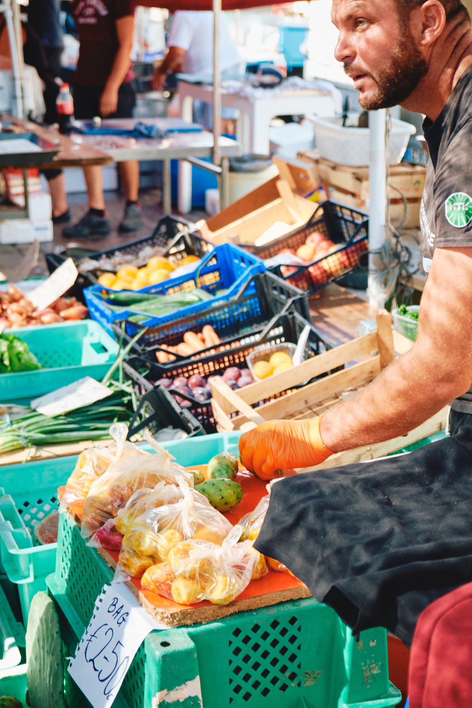 Vendor arranging fresh produce in colorful plastic crates at outdoor market.