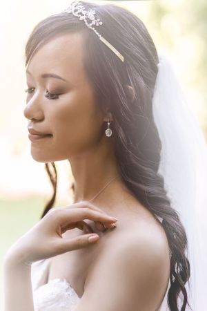 Bride in soft lighting wearing delicate tiara and drop earrings with natural makeup.