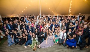 Large group wedding reception photo with guests celebrating under tent lighting.