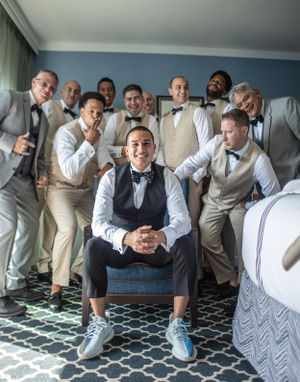 Groomsmen in light colored suits pose playfully for a group photo in a hotel room.
