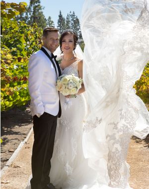 A romantic wedding photo featuring a flowing veil and white floral bouquet against autumn foliage.