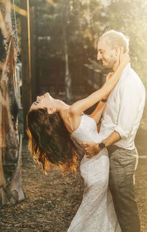 A romantic wedding photo of a couple embracing in golden sunlight among trees.