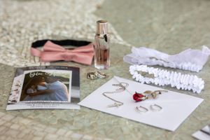 Wedding details flat lay with invitation, garter, and perfume bottle on textured surface.