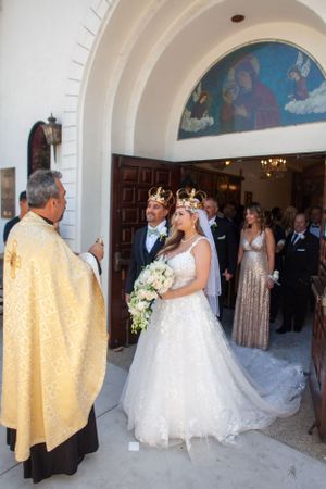 A traditional church wedding ceremony with priest in gold vestments and couple wearing crowns during Orthodox service.