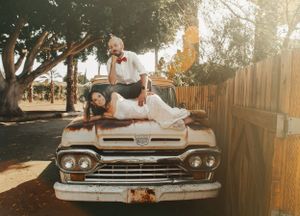 A playful couple poses on a vintage Chevrolet truck in warm sunset lighting.