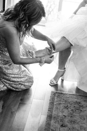 Bridesmaid helping the bride with her wedding shoe in black and white photography.
