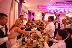 Wedding reception guests toasting and celebrating with drinks under pink mood lighting.
