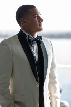 A groom in a classic white dinner jacket and bow tie looking pensively to the side.