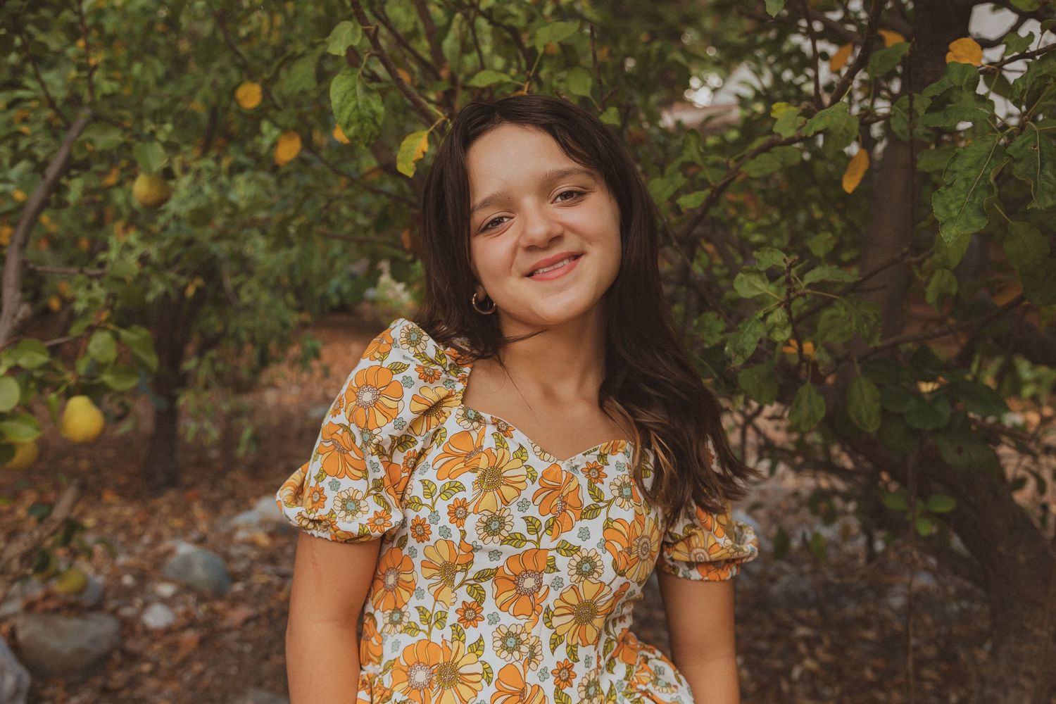 Portrait of someone in a floral dress standing among citrus trees.