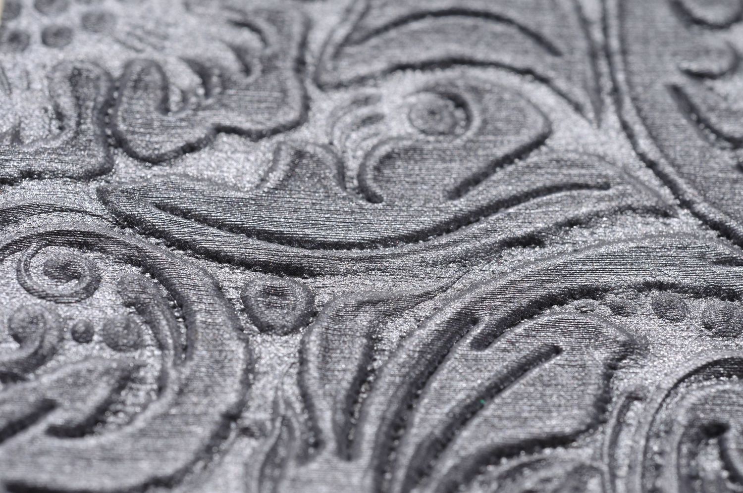 Close-up macro photograph of ornate swirling floral patterns embossed in gray metallic texture.