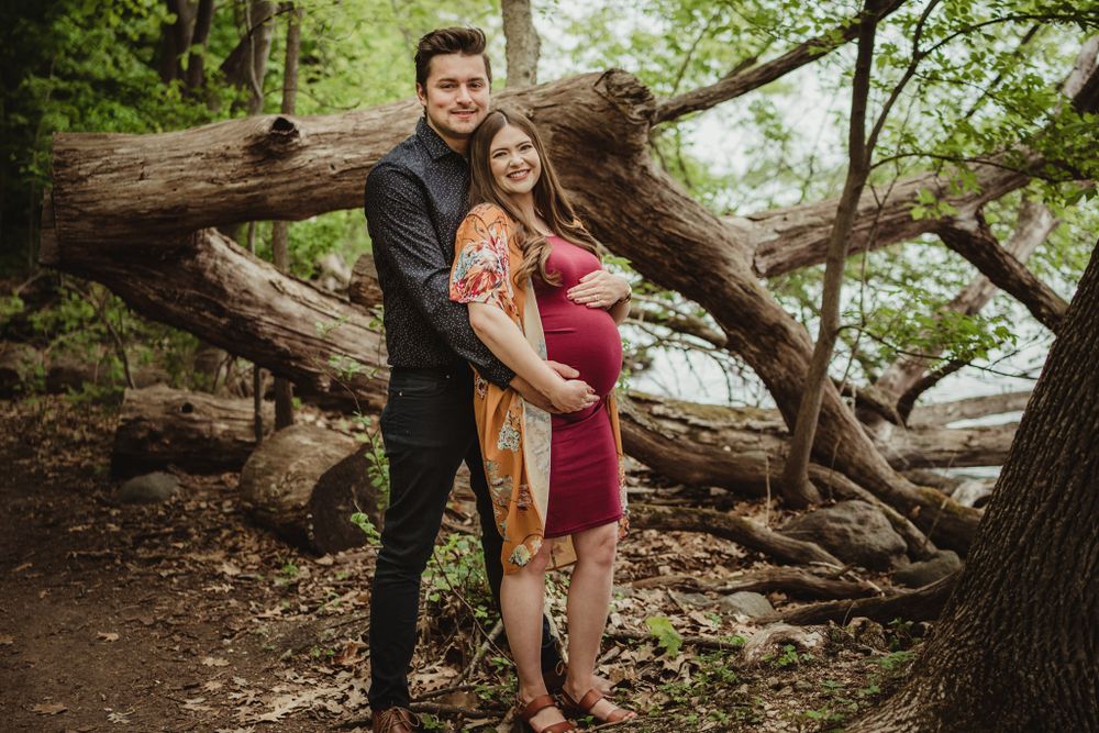 A couple poses for a maternity photo against fallen trees in a forest setting.